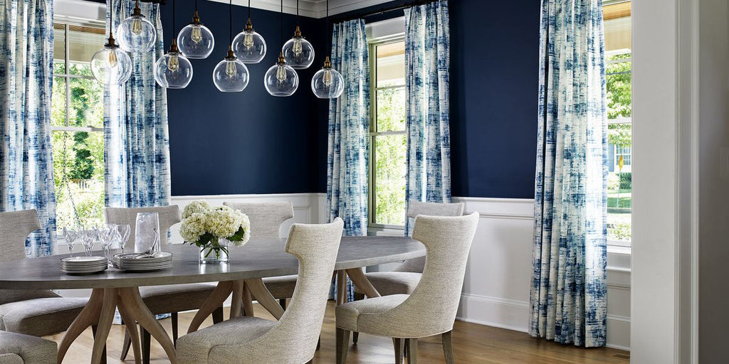blue and white dining room, navy and white design, navy walls, blue and white drapery fabric, white upholstered dining chairs, wood dining room table, glass globe pendant lighting, glass vase, modern decor, two-toned walls, navy grasscloth, toile
