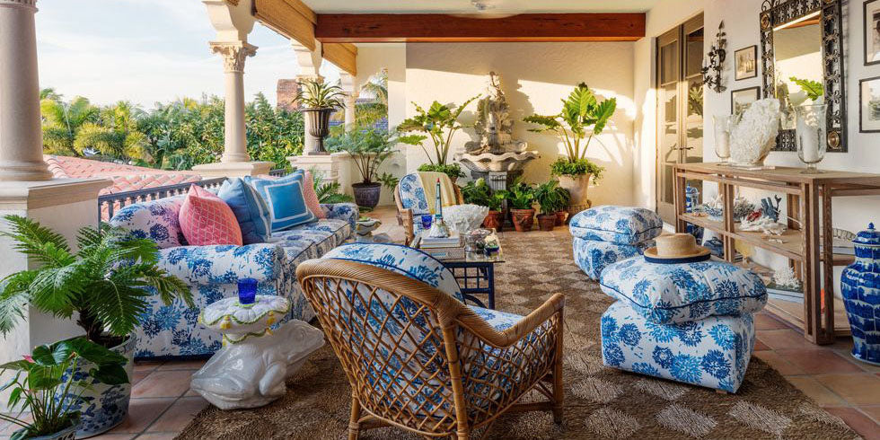 loggia with blue floral fabrics, kips bay palm beach 2019, outdoor living space, blue abstract upholstery fabric, blue upholstered ottomans, blue throw pillows, glass coffee table, metal framed mirror, white accent table, white decor, rattan chair