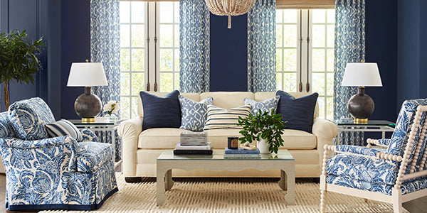blue and white design, navy walls, blue and white drapery, tan area rug, blue and white paisley upholstery fabric, tan coffee table, beaded pendant lighting, dark blue table lamp, glass coffee table, blue and white throw pillows, white accents