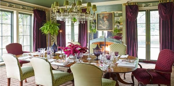 green and red dining room, richard keith langham dining room, veranda green dining room, elegant green dining room, burgundy drapery, green upholstered dining chairs, white candlesticks, red and white area rug, wooden dining table, green chandelier 