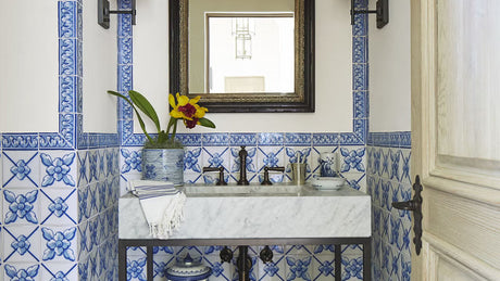 Blue and white tiled powder room with floral ceramic walls, marble sink, vintage sconces, blue wallpaper with a tile design