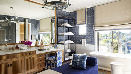 bathroom with blue ikat wallpaper, black etagere, wood vanity, blue upholstered chair