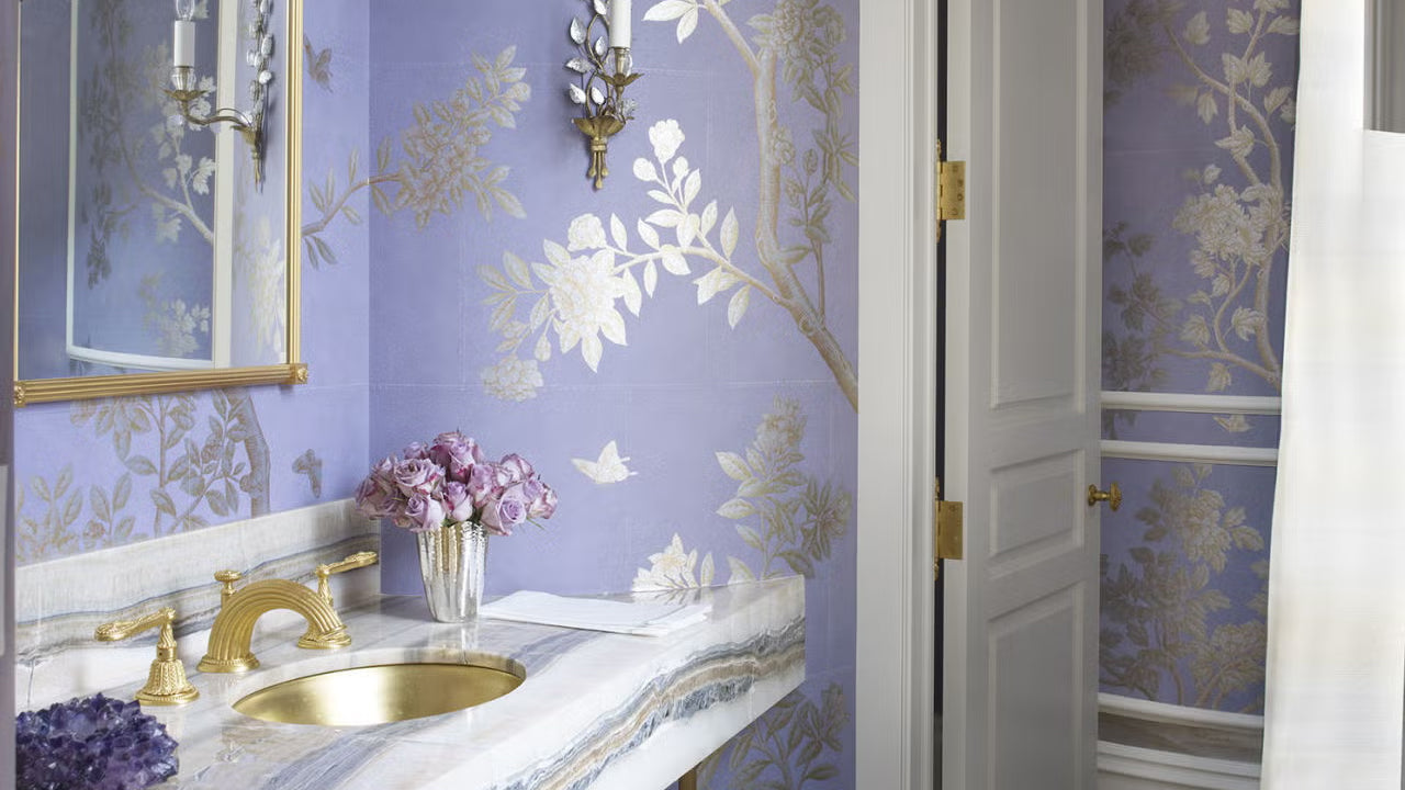 Lavender powder room with metallic floral wallpaper, marble vanity, gold sink and faucet, and brass sconces