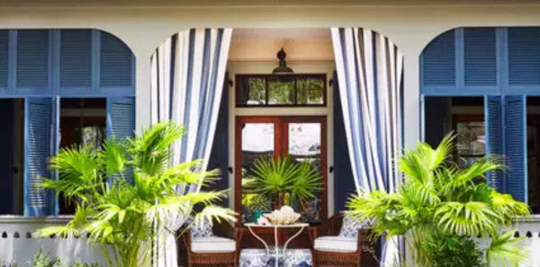 blue and white porch with drapery, blue shutters, southern living, white and blue design, outdoor living, white metal outdoor table, rattan chairs, outdoor decor, white serving dish, blue and white striped drapery, green ferns, black metal lighting