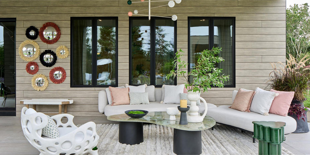 contemporary outdoor living room, organic curved sofa, curved coffee table, holiday house hamptons, white outdoor fabric, white outdoor area rug, mirror wall art, white and black chandelier lighting, white accent chair, pink white and grey pillows