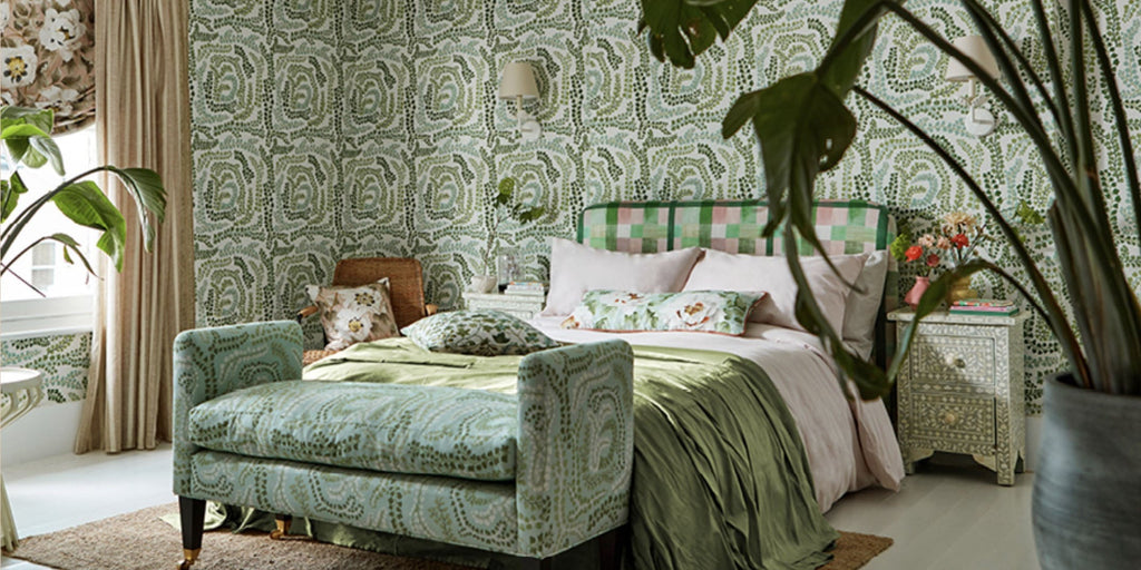 green bedroom, green wallpaper, harlequin colours 4, harlequin fayola wallpaper, harlequin wallpaper, upholstered bench seating, green abstract fabric, upholstered headboard, neutral drapery, abstract floral wallpaper, brown area rug, floral drapes