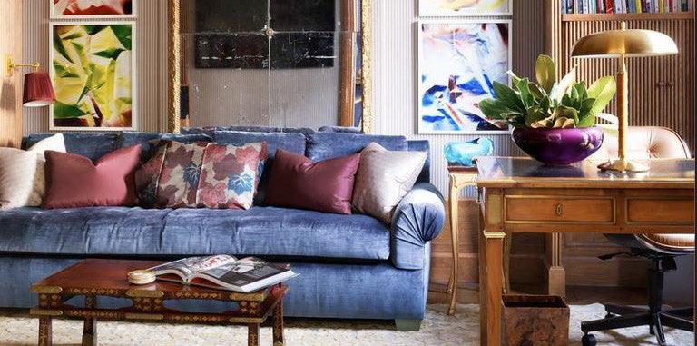 blue velvet sofa, stephen sills home office, purple pillows, gold table lamp, wooden coffee table, home office, library, neutral area rug, gold and purple sconce lighting, silver throw pillows, abstract colorful wall art, wood framed mirror, office