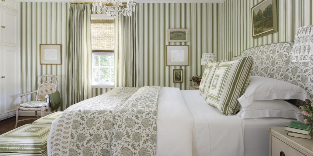 green stripe wallpaper, green stripe drapery, coordinating wallpaper and fabric, green floral bedding, green striped pillows, green striped stools, wall art, glass pendant lighting, rattan chair, ikat fabric, upholstered headboard, green blanket
