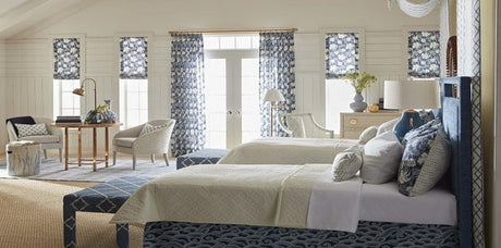 A blue and white guest bedroom by Sarah Richardson, blue and white design, blue floral drapery fabric, navy and white bench, upholstered bed, geometric accent wall, grey accent chairs, blue and white throw pillows, navy throw blanket, white bedding