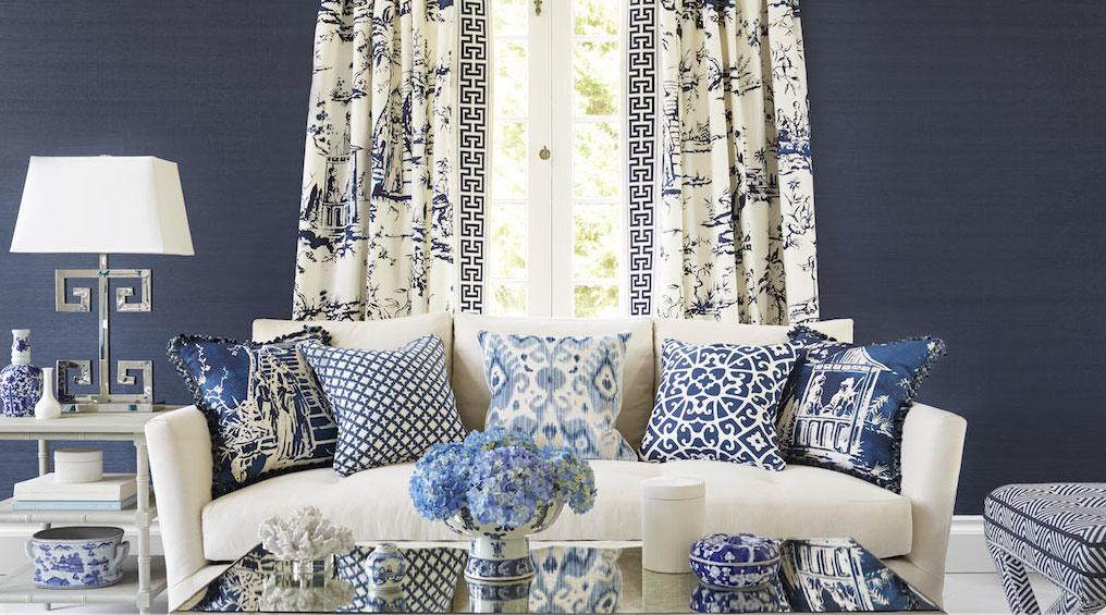 Blue and White Living Room with Asian Inspired fabrics, assorted blue pillows, white upholstery, navy walls, toile drapery, mirror coffee table, asain inspired patterns, silver greek key table lamp, greek key trim, blue and white design, side tables
