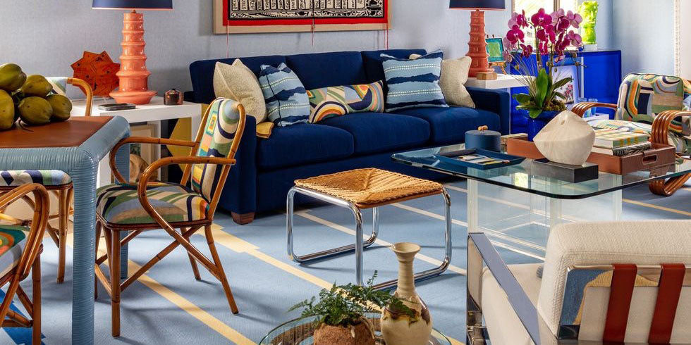 coastal living room, navy sofa, vintage furniture, scott sanders kips bay palm beach showhouse, dark blue upholstery, blue table, abstract upholstered dining chairs, glass coffee table, blue and white striped area rug, orange table lamp, wall art