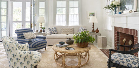 blue floral fabric, blue striped upholstery, beige geometric area rug, bronze table lamps, rattan coffee table, earth tones, white drapery, blue geometric fabric, blue and beige throw pillows, blue decor, blue and white design, blue living room