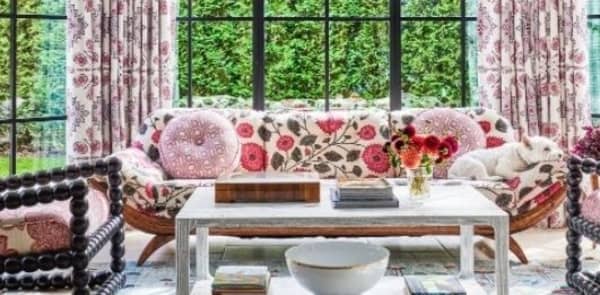 Floral sunroom, floral indoor/outdoor room, pink floral room, white coffee table, coordinating wallpaper and fabric, floral upholstered sofa, upholstered chairs, pink throw pillows, pink design, wood coffee table, white bowl decor, floral area rug