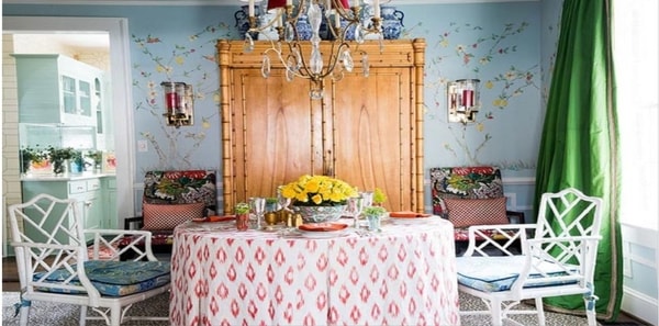 grand millenial dining room, blue floral wallpaper, ikat fabric, white bamboo style furniture, glass chandelier, green draperies, blue floral seat cushions, grand millenial wallpaper, colorful grand millenial design, white and pink ikat tablecloth