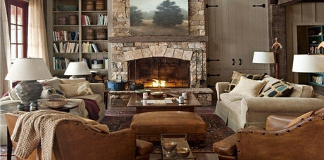 Cabincore, winter decor, white sofa, stone, leather, wood panels, cabincore living room, rustic cabincore earth tones, stone fireplace, brown upholstered ottoman, grey table lamps, traditional area rug, light brown throw blanket, earthy accent decor