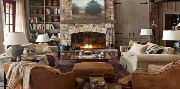 Cabincore, winter decor, white sofa, stone, leather, wood panels, cabincore living room, rustic cabincore earth tones, stone fireplace, brown upholstered ottoman, grey table lamps, traditional area rug, light brown throw blanket, earthy accent decor