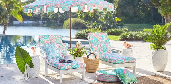 Pool chairs covered in Lilly Pulitzer fabric, lilly pulitzer, colorful outdoor fabric, poolside design, matching umbrella and chair, tropical design,  blue and pink throw pillow, white ceramic side tables, white ceramic planter, tropical pouf