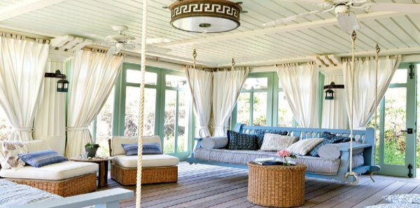 blue porch, blue sunroom, swinging chair, blue indoor outdoor pillows, blue indoor outdoor rug, rattan table, wicker table, rope table, swinging sofas, white draperies, metal flush lighting, white outdoor fan light, outdoor grey area rug, rattan